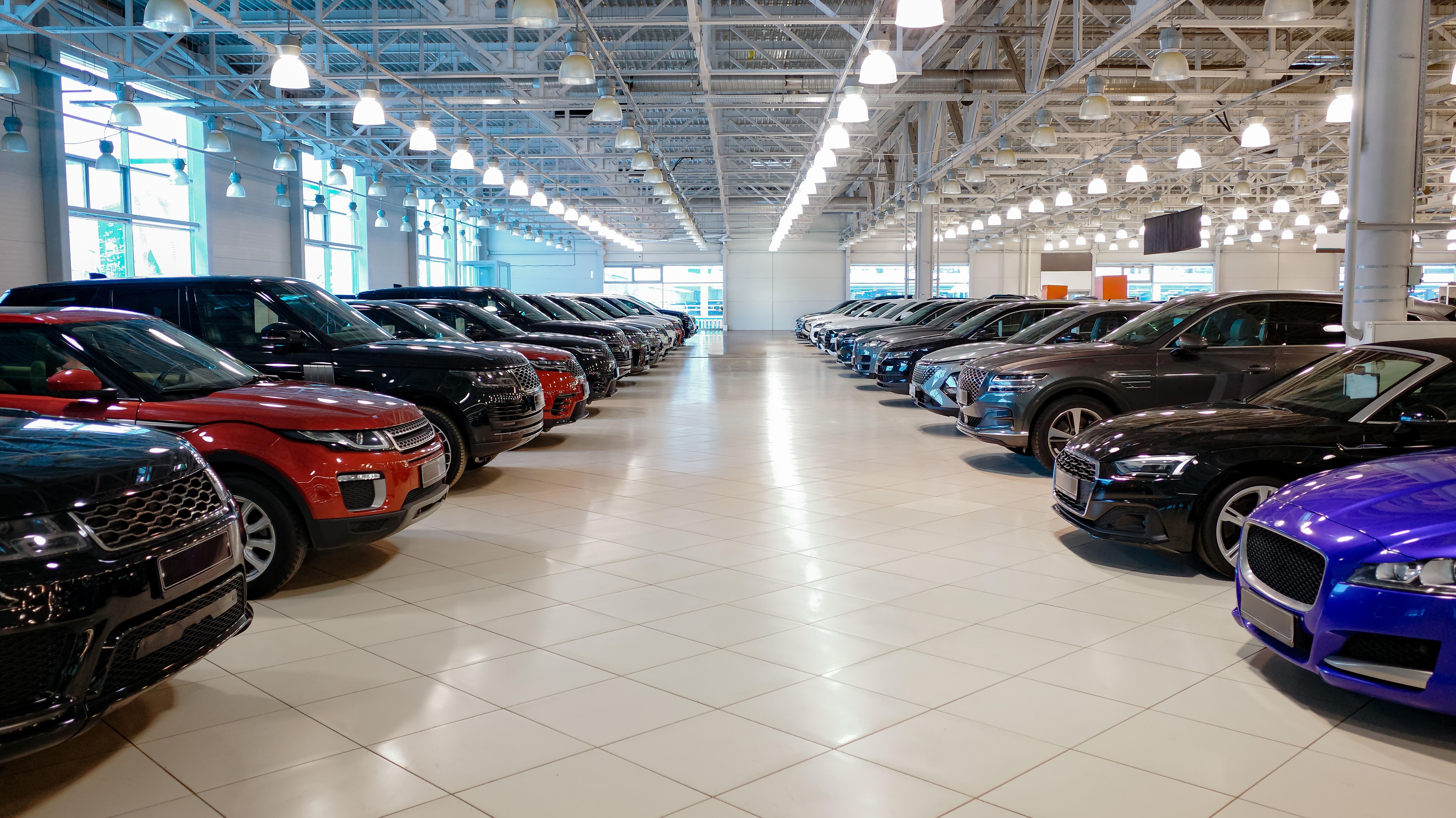 Spacious modern car showroom with multiple vehicles parked in rows under bright ceiling lights, dealership interior concept for automotive retail and sales.